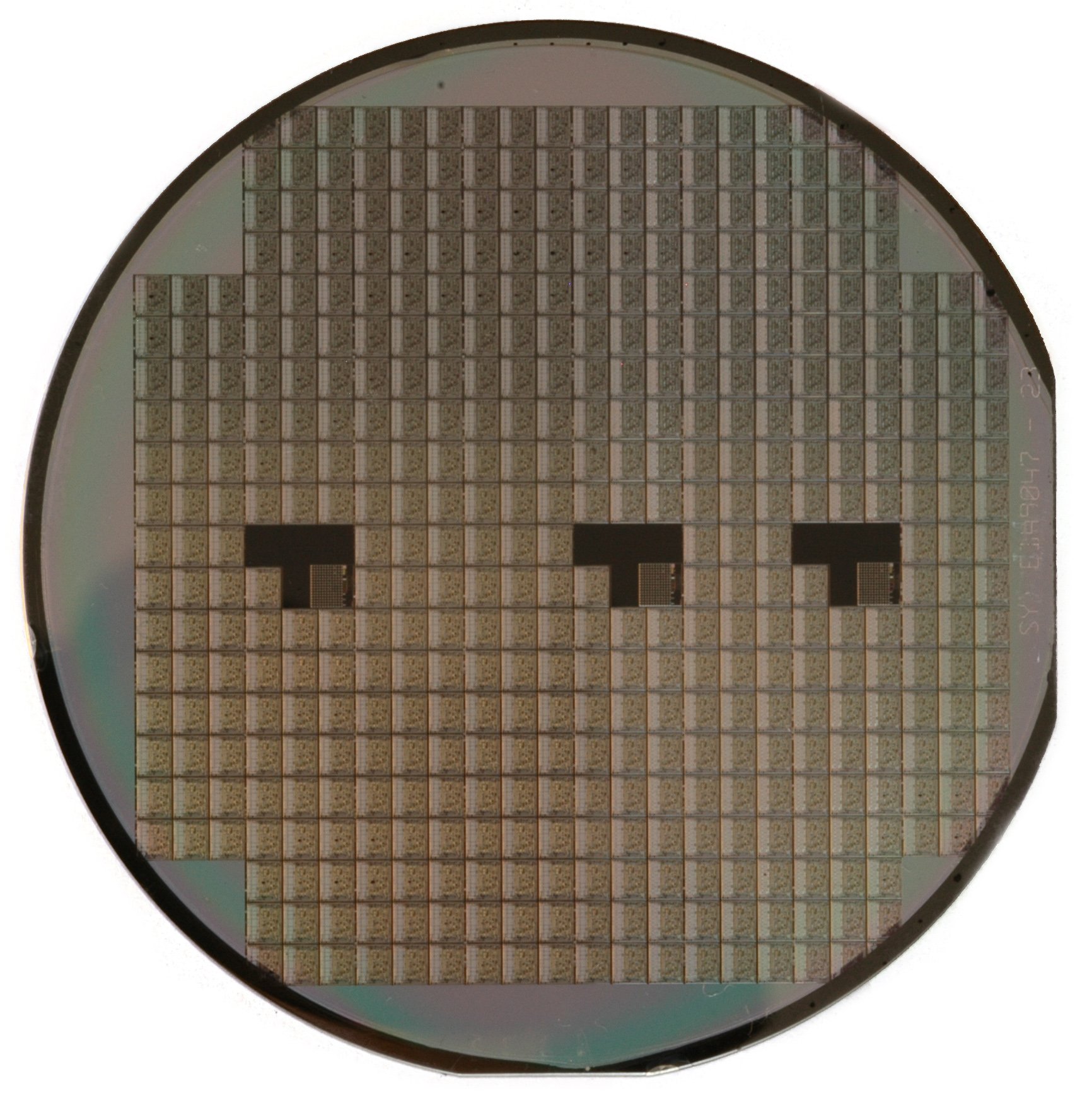 A polished silicon wafer covered in a grid of rectangular chips, three dark squares visible among them