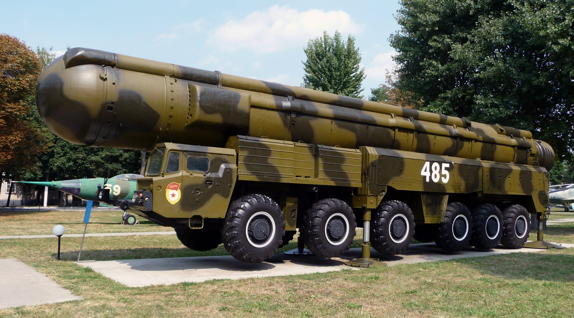 A camouflaged transporter-erector-launcher carrying a large missile stands on grass, its serial number painted on the cab