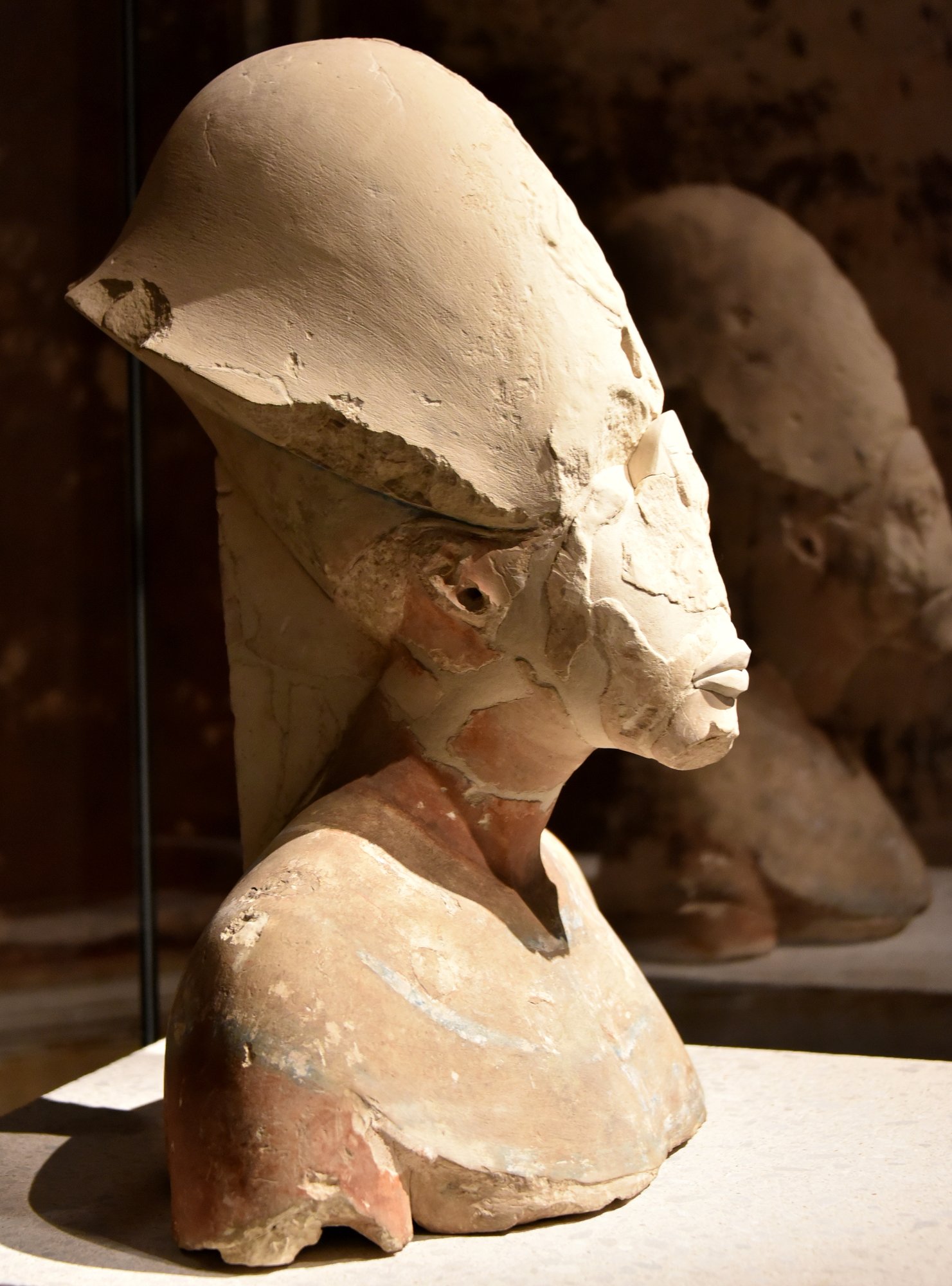 Plaster portrait head of Akhenaten with an elongated face, displayed in a dark museum case
