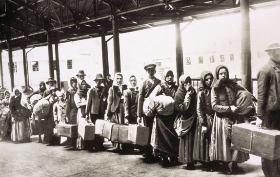 Historic photograph of emigrants with bundles and cases waiting in a long queue in a covered inspection hall