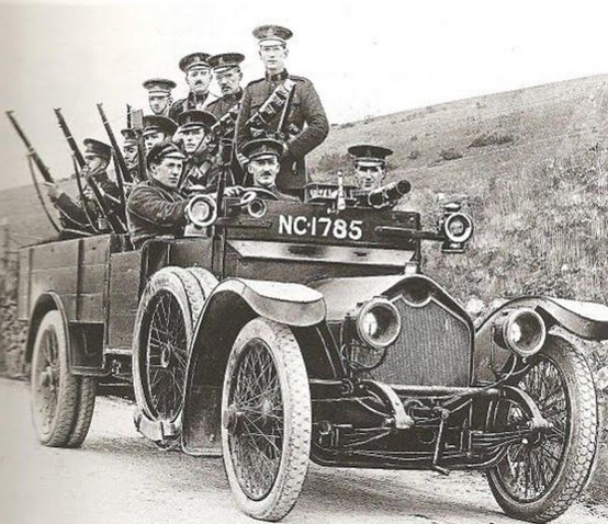 Historic photograph of uniformed men with rifles crowded onto an open motor car on a hillside road